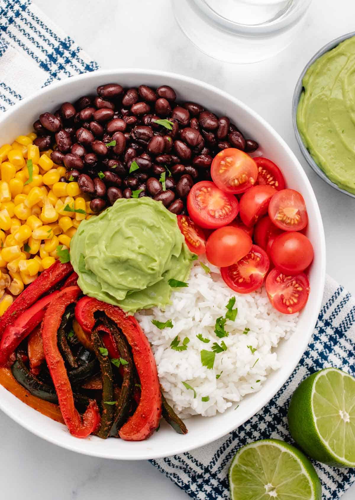 Veggie fajita bowl with rice, black beans, corn, cherry tomatoes, and avocado lime crema.