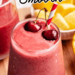 A cherry mango smoothie in a glass with a straw and two cherries.