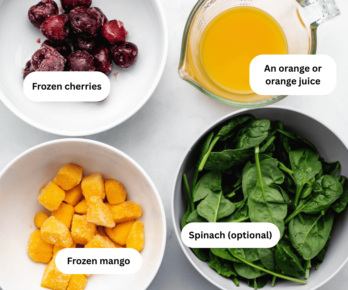 A bowl of cherries, orange juice, frozen mango, and spinach.