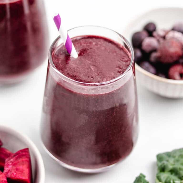 A kale beet smoothie in a glass with a straw.