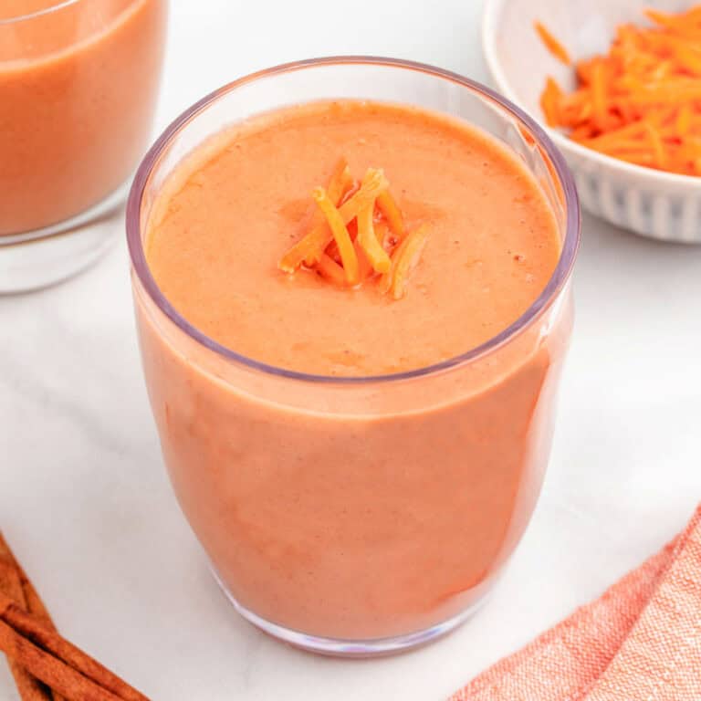 A carrot banana smoothie in a glass with shredded carrots on top.
