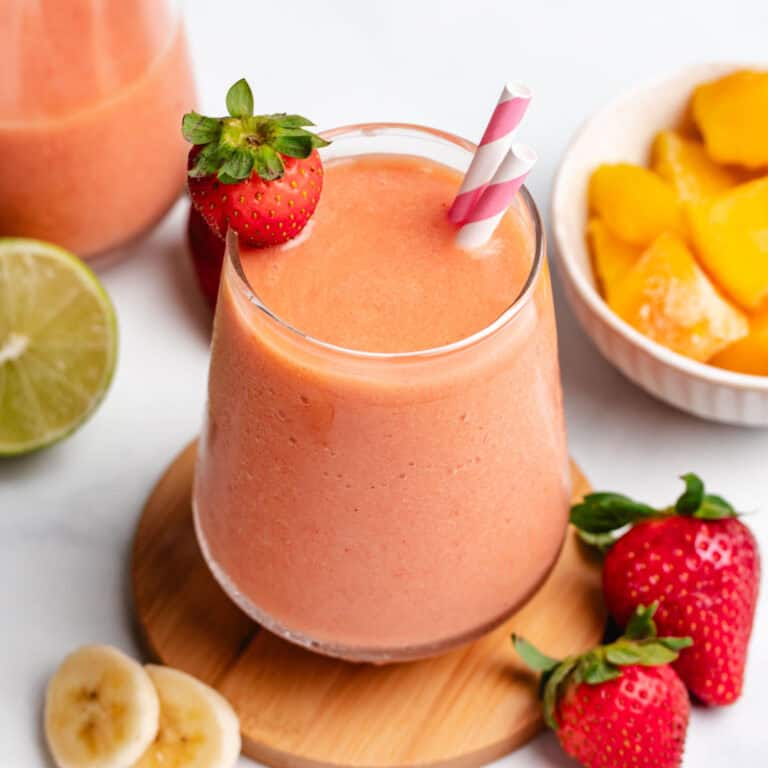 Mango strawberry banana smoothie in a glass with straws and a fresh strawberry.