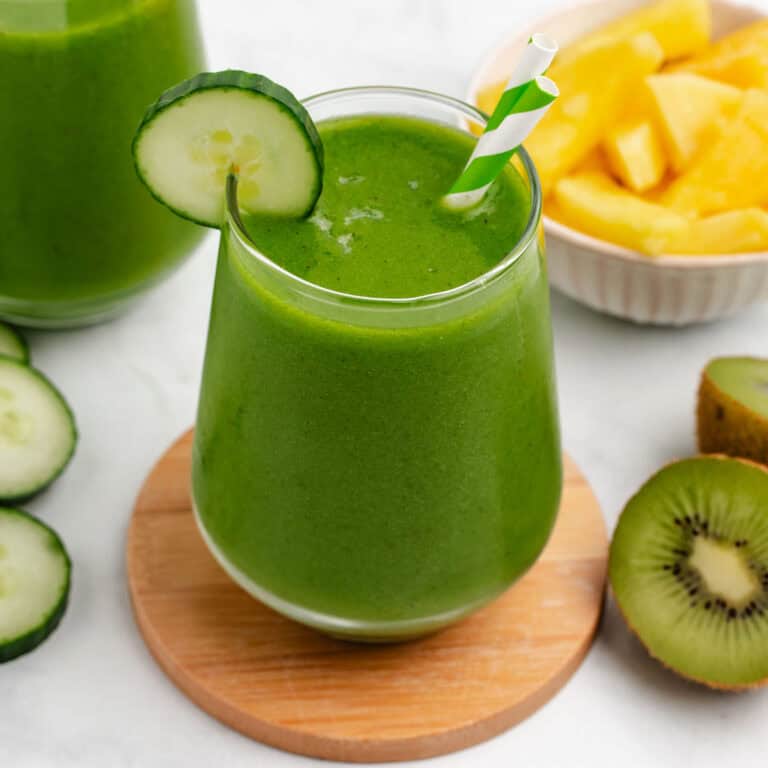 Pineapple cucumber green smoothie in a glass with a straw and a cucumber slice.