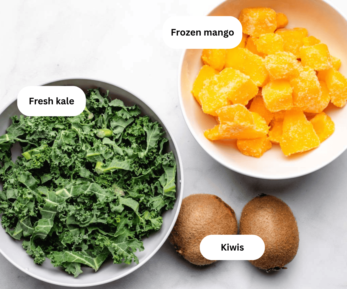Frozen mango, fresh kale, and two kiwis on a table.