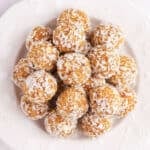 Carrot cake bliss balls covered in shredded coconut on a plate.
