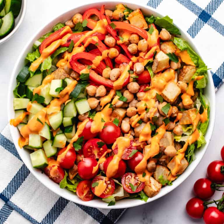 A bowl with chickpeas, red bell peppers, potatoes, cherry tomatoes, cucumbers, and a roasted red pepper dressing.