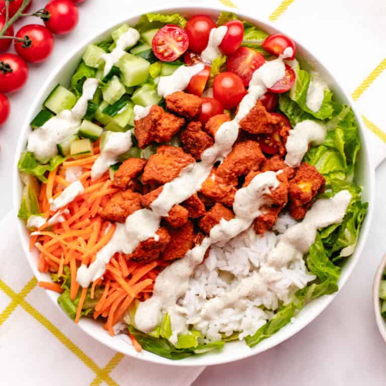 A bowl with buffalo tofu bites, rice, cherry tomatoes, cucumbers, shredded carrots, lettuce, and vegan ranch dressing.