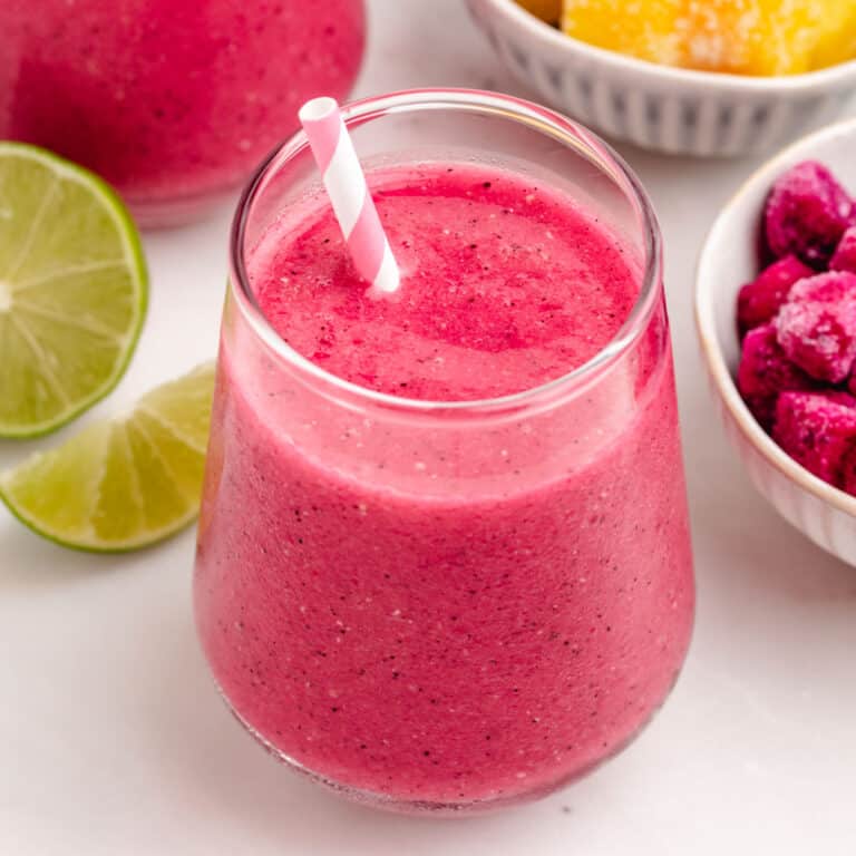 A dragon fruit smoothie with mango in a glass with a straw.