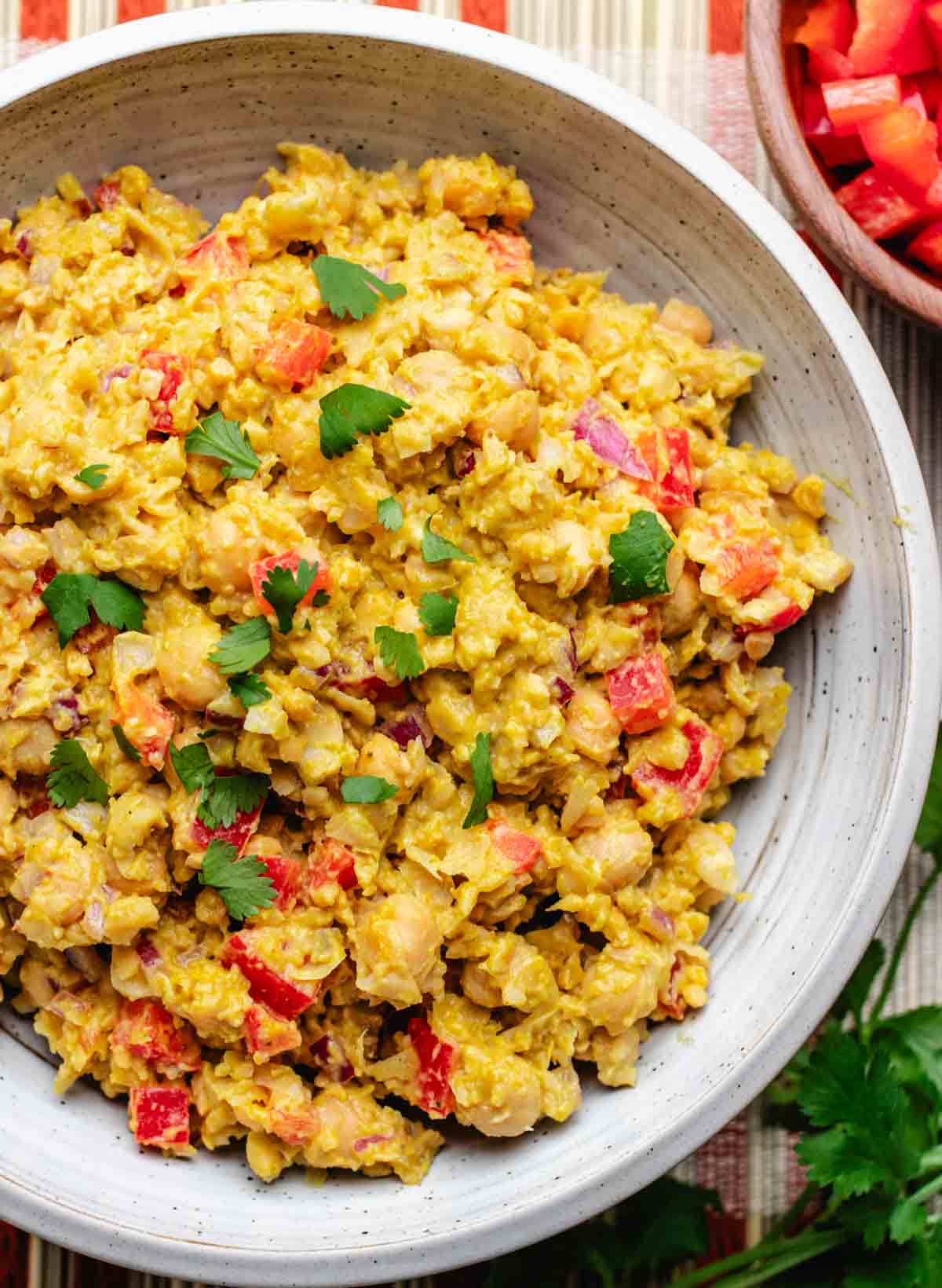 Vegan chickpea curry salad in a bowl with diced red bell peppers and chopped cilantro.