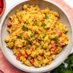 Vegan curry chickpea salad in a bowl with diced red bell peppers and chopped cilantro.