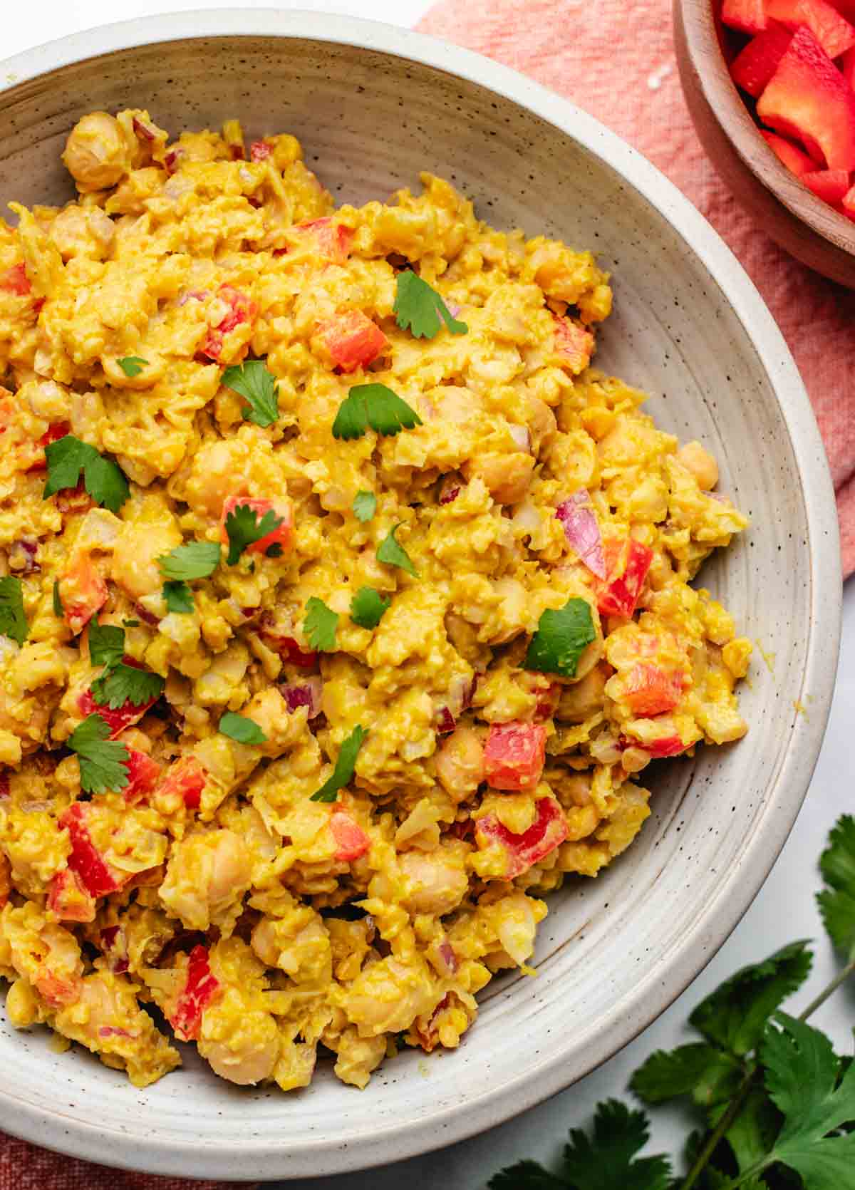 Vegan curry chickpea salad in a bowl with red bell peppers and chopped cilantro.
