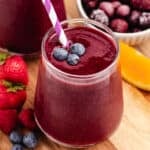 A red beet spinach smoothie with berries and orange slices.