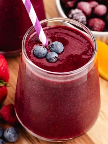 A red beet spinach smoothie with berries and orange slices.