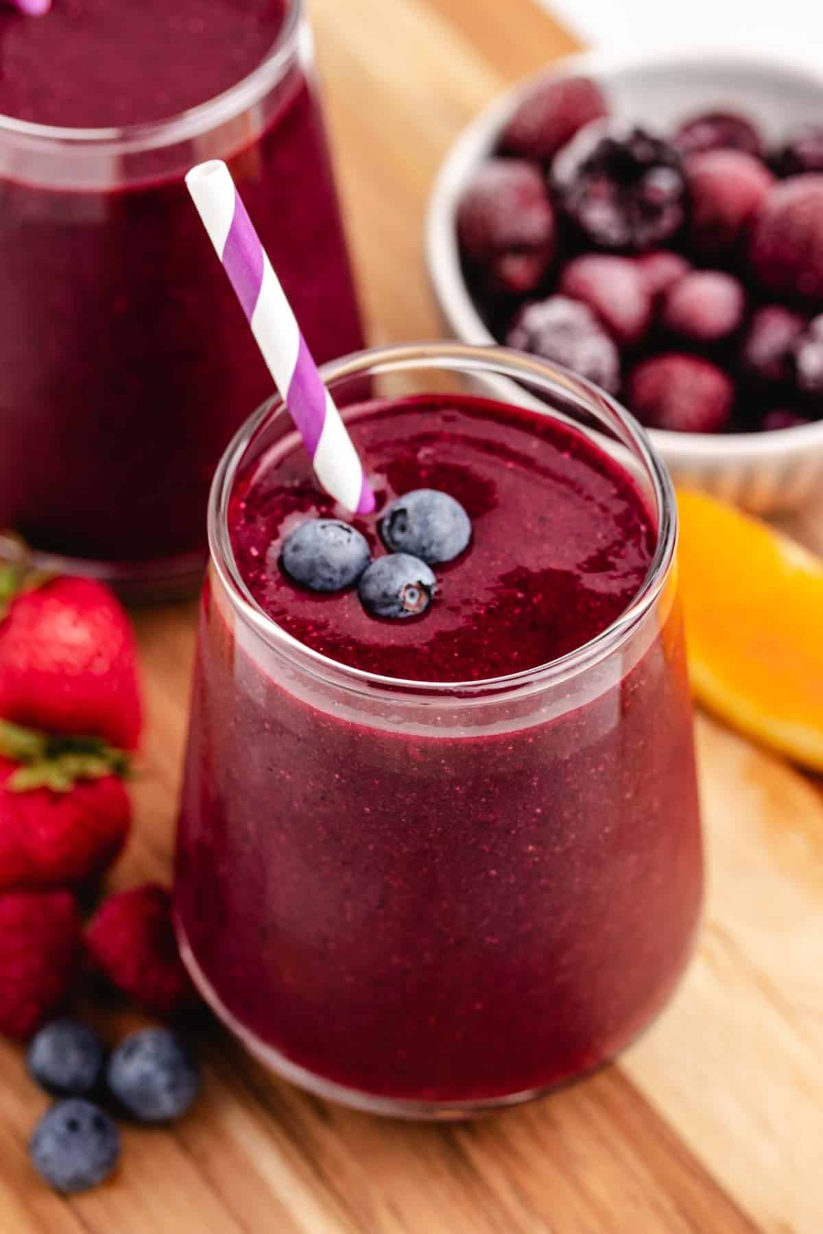 A beetroot spinach smoothie in a glass with a straw and blueberries on top.