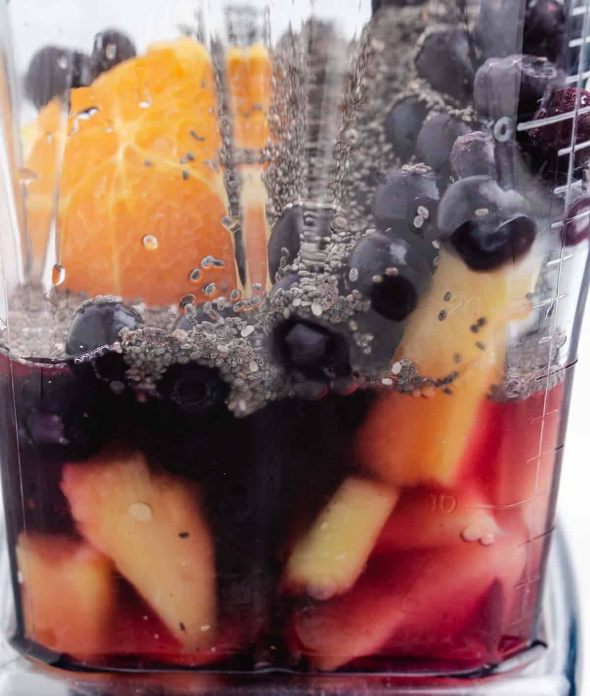 Frozen blueberries, frozen pineapple, chia seeds, an orange, and water in a blender.