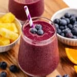 A blueberry pineapple smoothie in a glass with a straw and fresh blueberries.