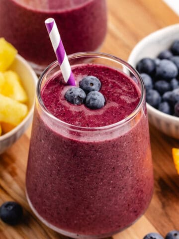 A blueberry pineapple smoothie in a glass with a straw and fresh blueberries.