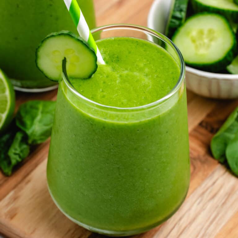 Cucumber spinach smoothie in a glass with a straw and a cucumber slice.