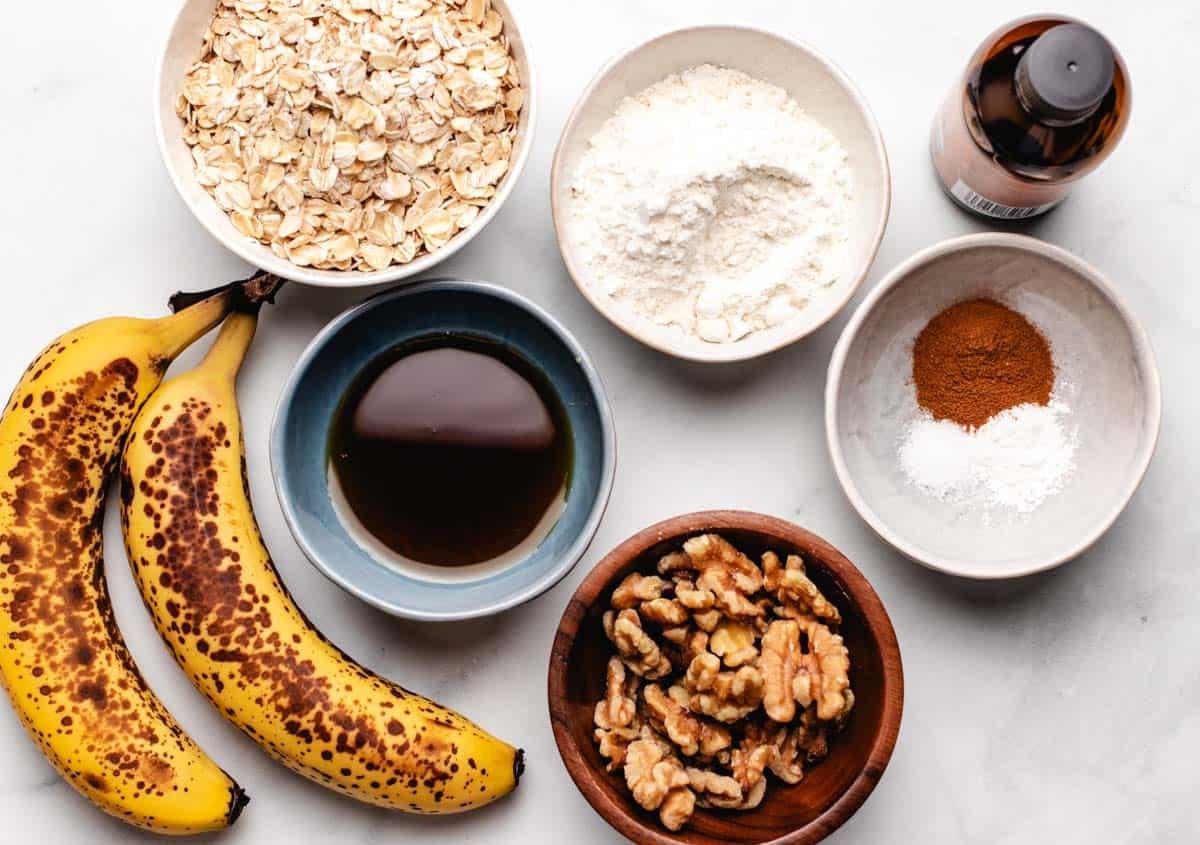 A bowl of rolled oats, oat flour, vanilla extract, ripe bananas, maple syrup, walnuts, ground cinnamon, baking powder, and salt.