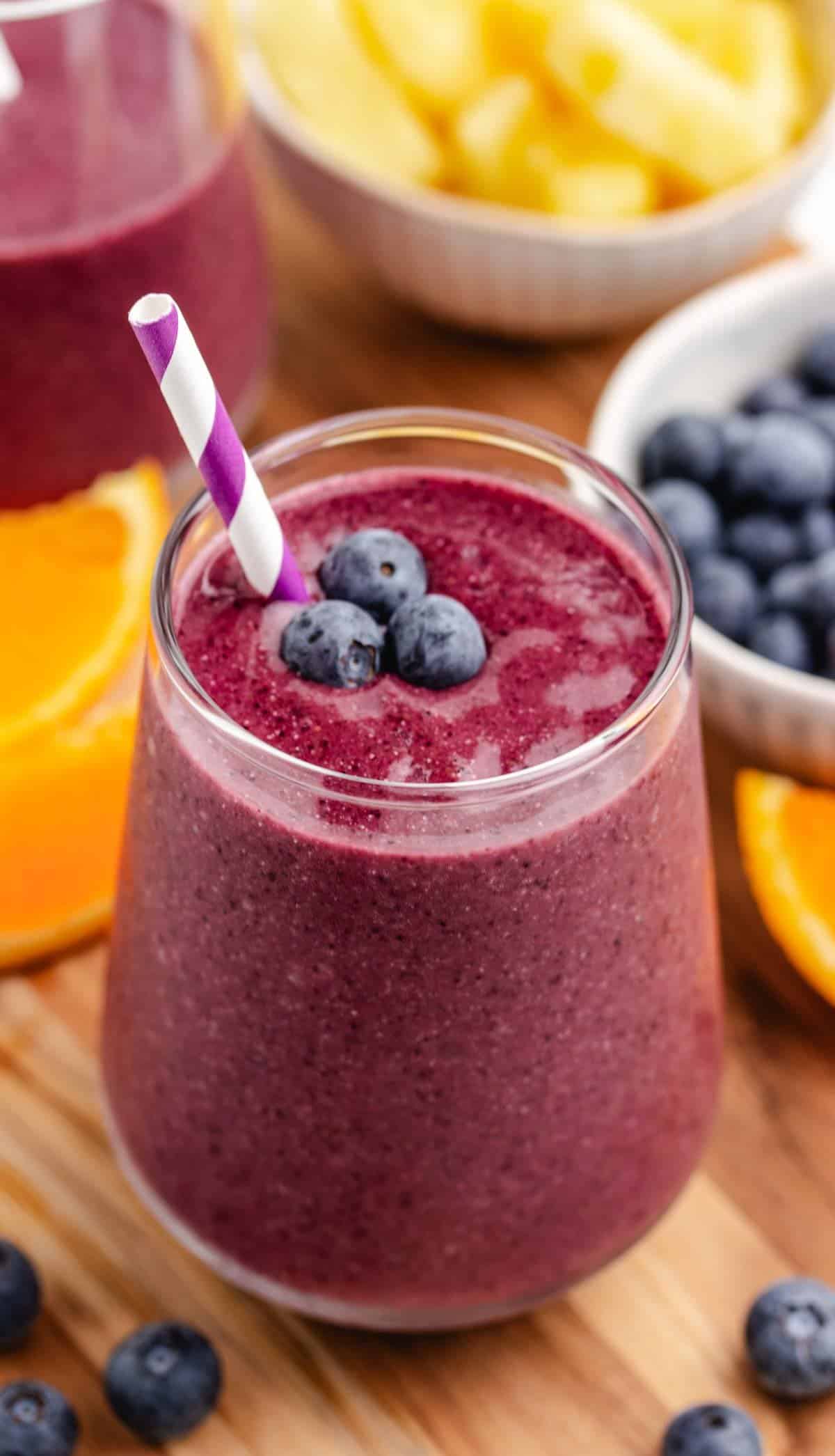 A pineapple and blueberry smoothie in a glass with a straw and fresh blueberries on top.