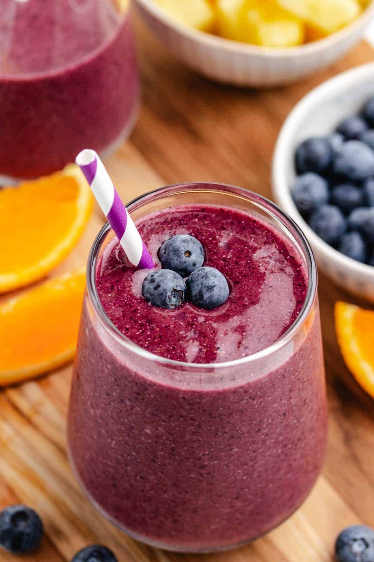 A pineapple blueberry smoothie in a glass with a straw and blueberries on top.