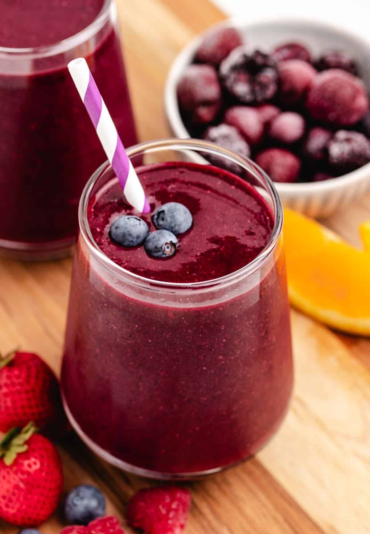 A spinach and beet smoothie in a glass with a straw and berries, and orange slices.