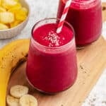 Beet and banana smoothie in a glass with a straw and a banana.