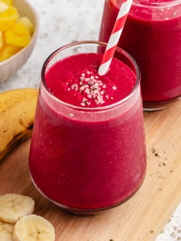 Beet and banana smoothie in a glass with a straw and a banana.