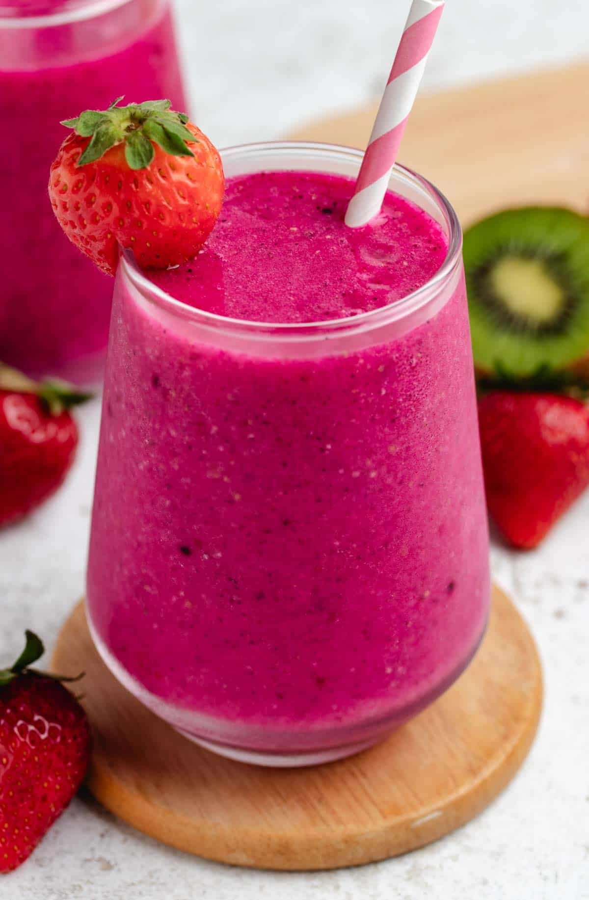 Strawberry dragon fruit smoothie in a glass with a straw and a strawberry.