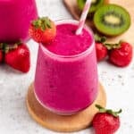 A dragon fruit strawberry smoothie in a glass with a straw and a strawberry.