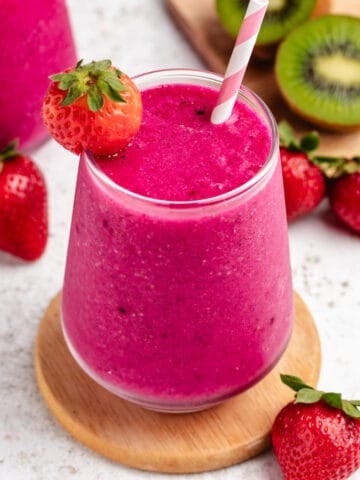 A dragon fruit strawberry smoothie in a glass with a straw and a strawberry.