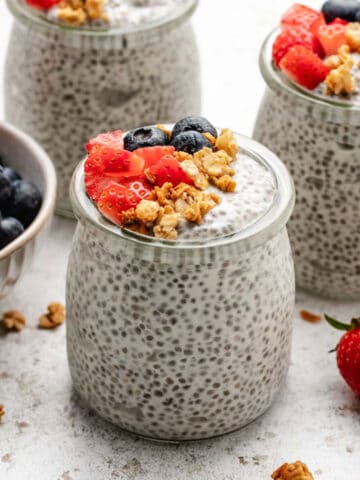 Yogurt chia seed pudding in a glass jar with granola, diced strawberries, and blueberries.