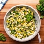 Pineapple corn salsa in a bowl with a spoon and sliced jalapeno.