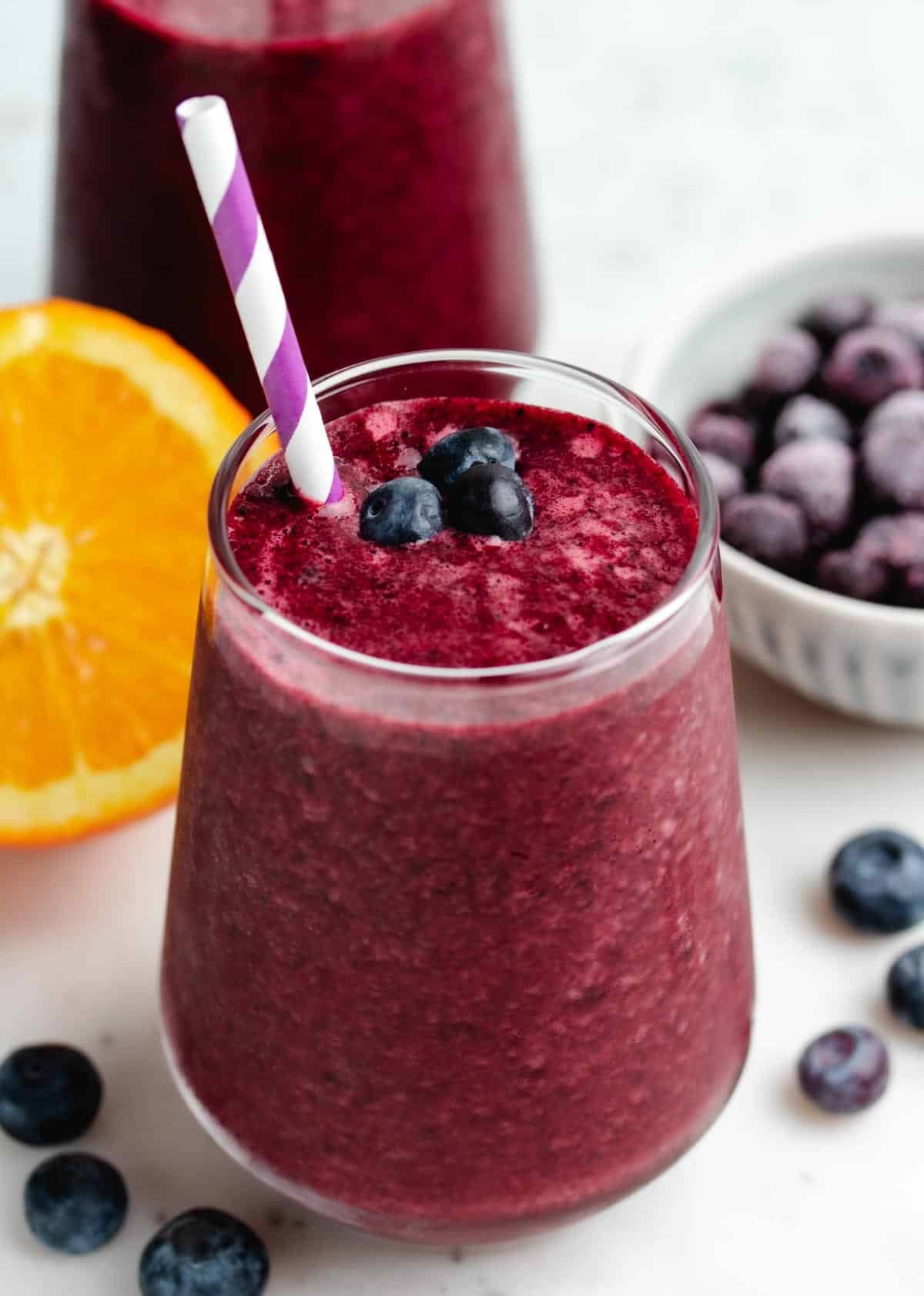 Blueberry beet smoothie in a glass with a straw and blueberries.