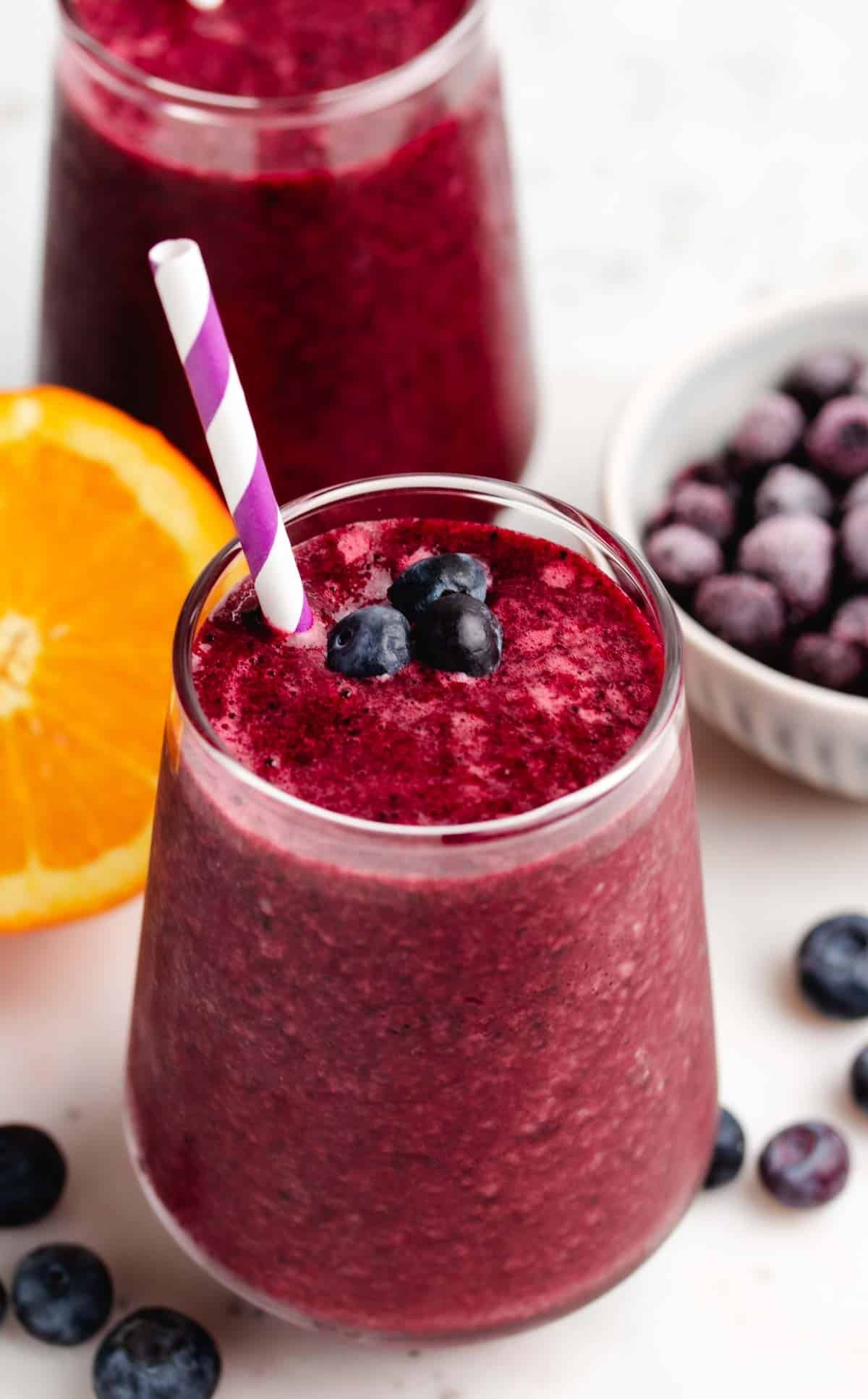 Blueberry and beet smoothie in a glass with a straw and blueberries on top.