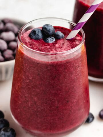 Beet and blueberry smoothie in a glass with a straw and blueberries on top.