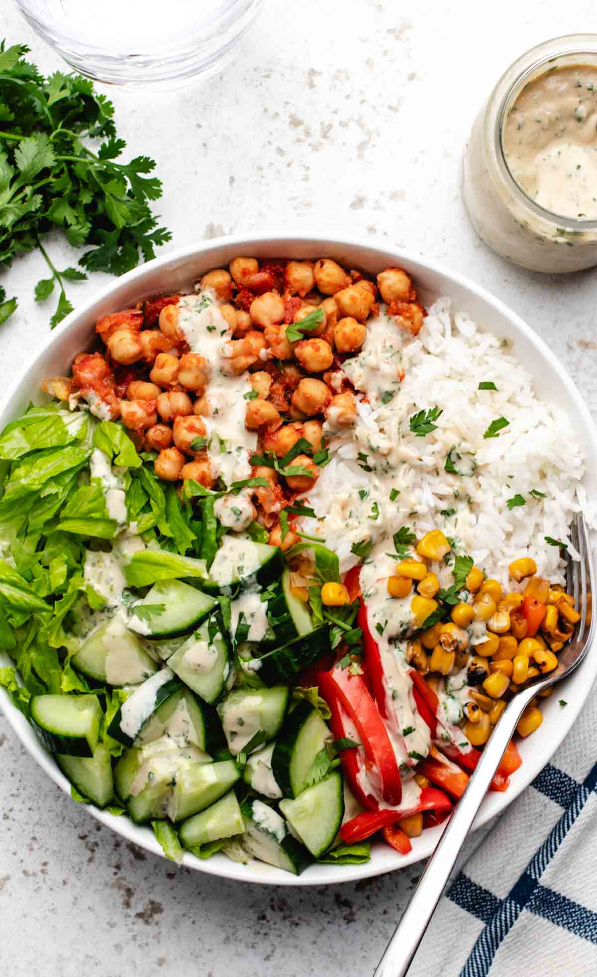 Chickpea bowl with corn, red bell peppers, lettuce, rice, and lime tahini dressing.