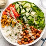 Chickpea Buddha bowl with tahini dressing, rice, cucumbers, red bell peppers, corn, and lettuce in a bowl.