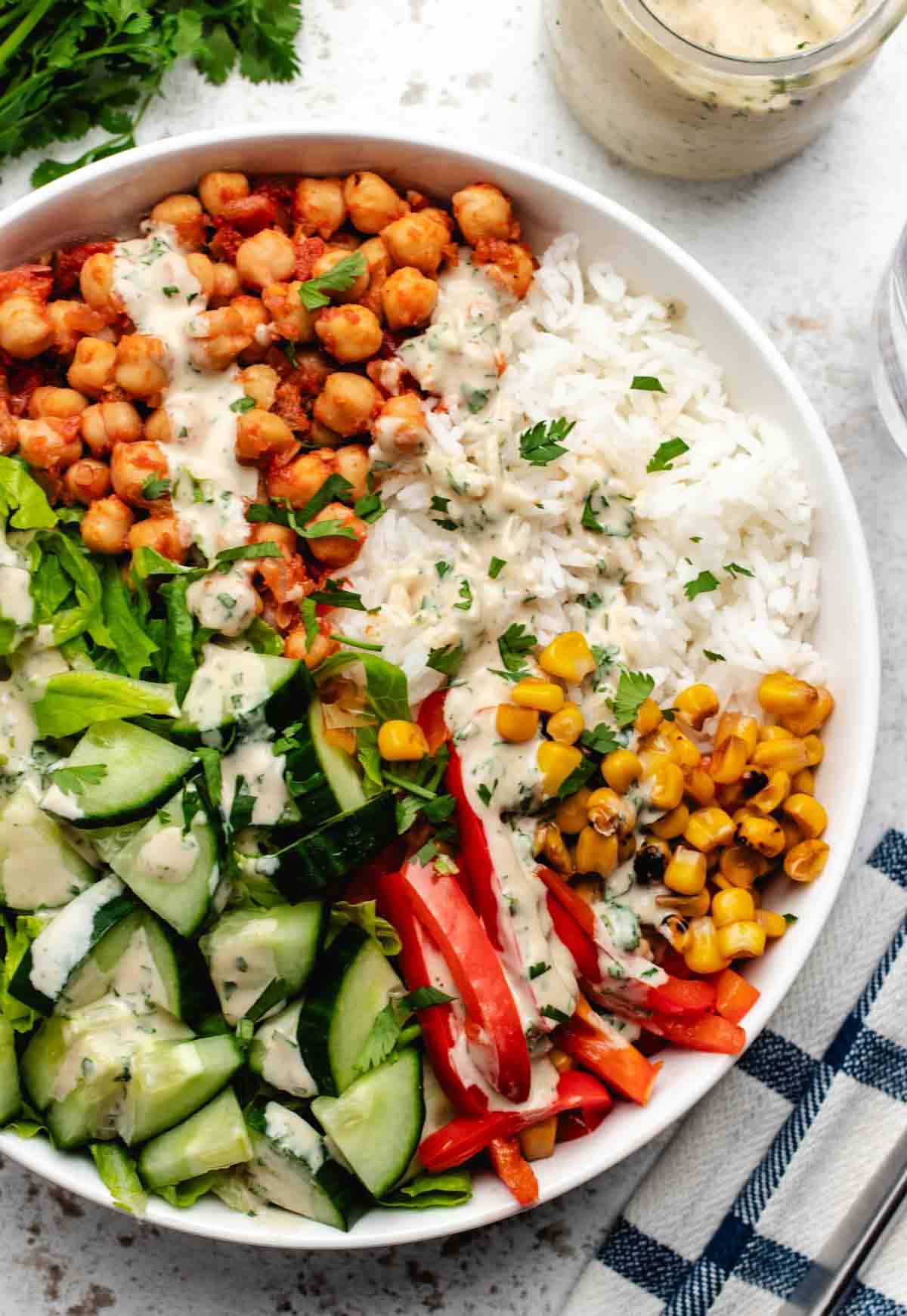 A chickpea Buddha bowl with tahini dressing, rice, cucumber, red bell peppers, corn, and lettuce.