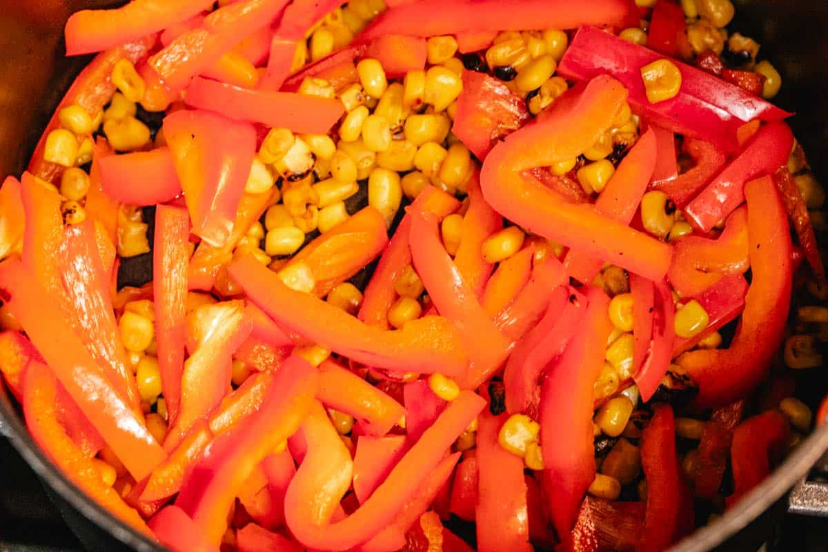 A saucepan with red bell peppers and corn.