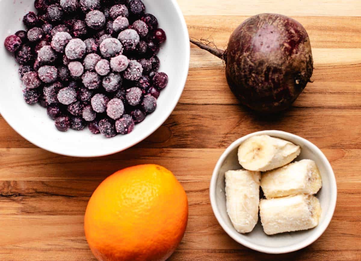 Frozen blueberries in a bowl, a beet, an orange, and a bowl of frozen banana.