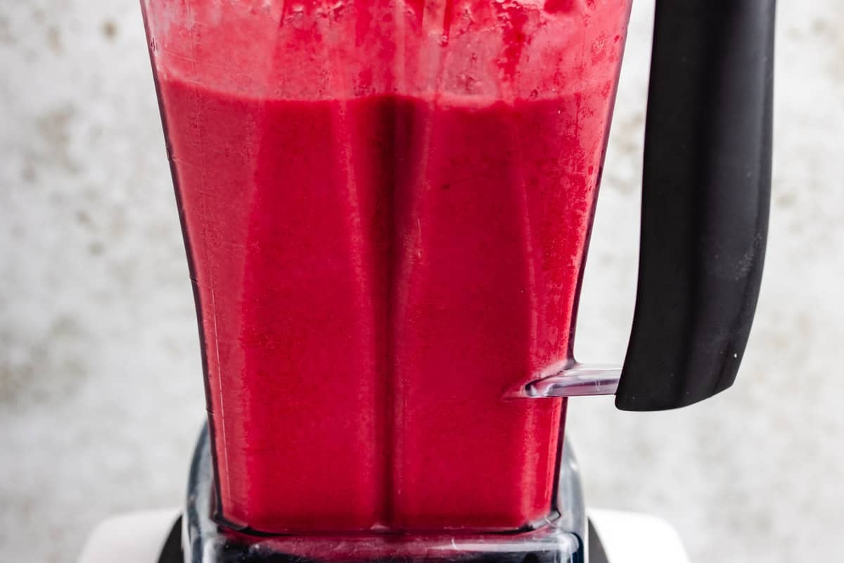 A smoothie blended in a blender made from beets, carrots, orange, banana, and frozen pineapple.