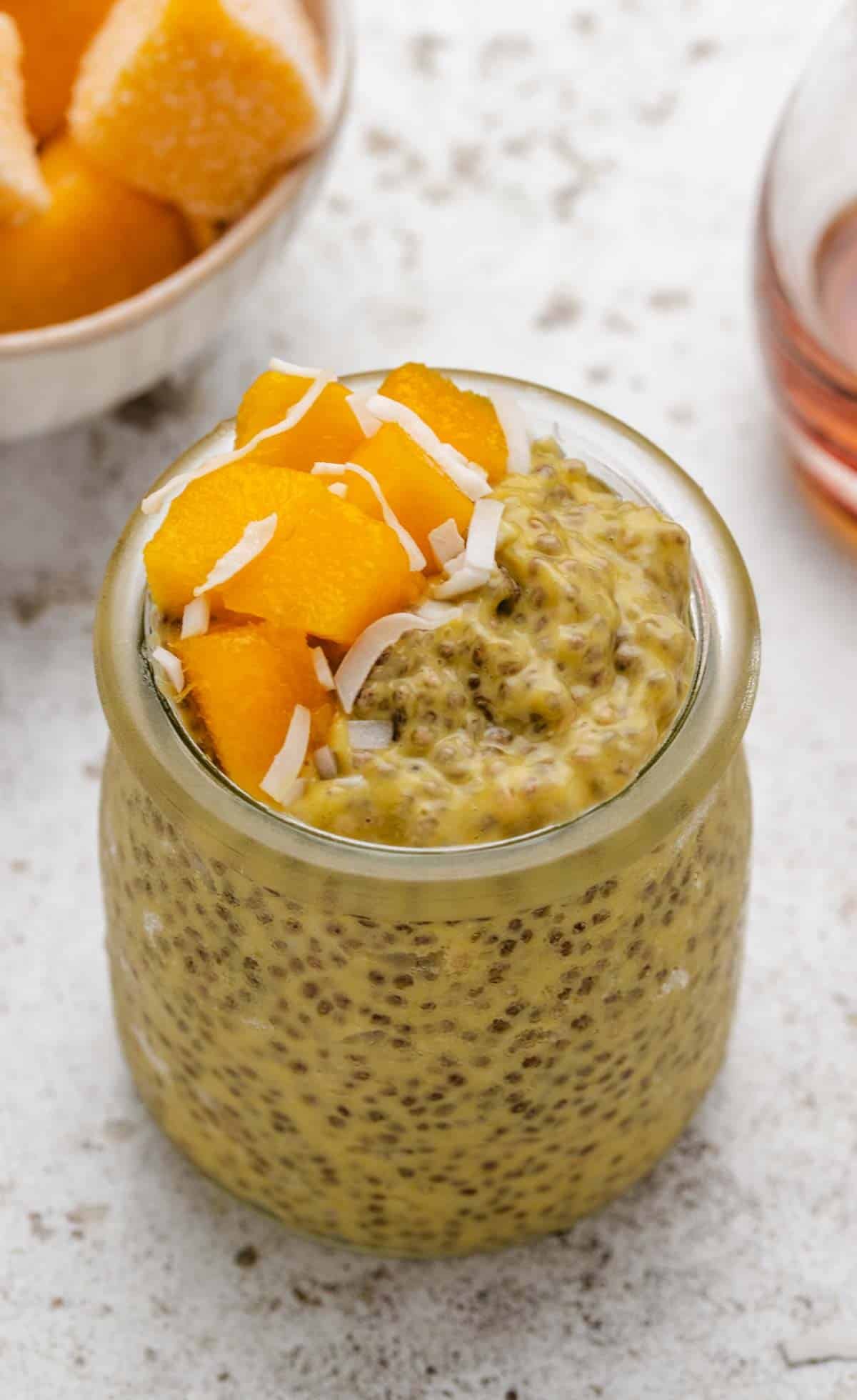 Mango chia pudding with yogurt in a glass jar with mango on top.