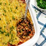 Mushroom lentil shepherd's pie in a baking dish with a spoon and chopped parsley on top.