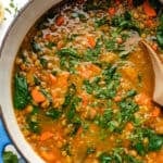 Carrot butternut squash soup in a large pot with chopped cilantro on top and a wooden spoon.
