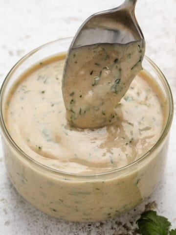 Lemon herb tahini in a glass with a spoon dipped in the dressing.