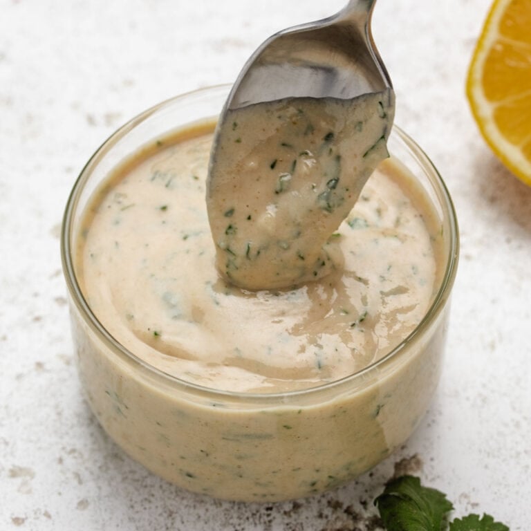 Lemon herb tahini in a glass with a spoon dipped in the dressing.