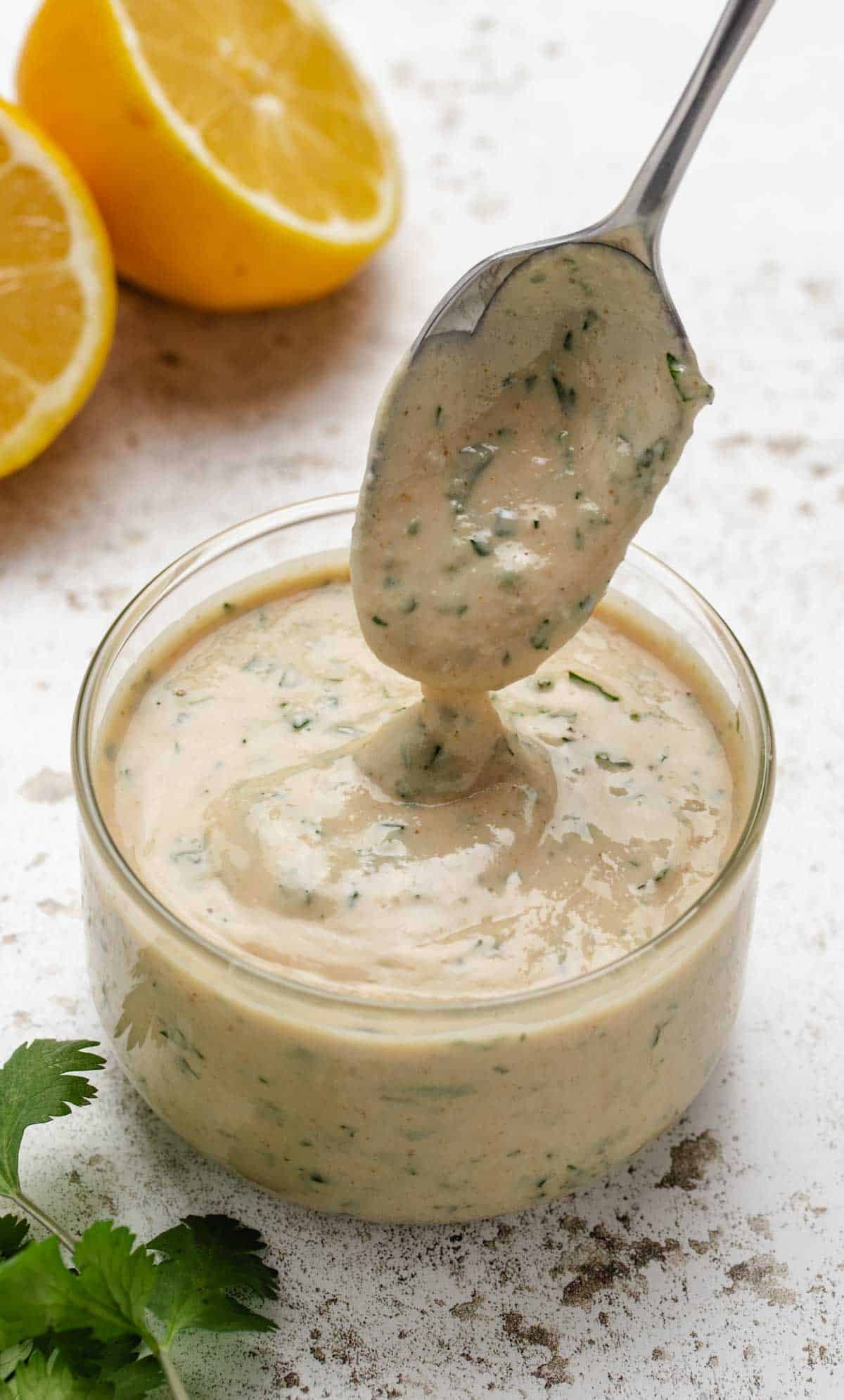 Lemon herb tahini dressing in a glass jar with a spoon dipped in the sauce.