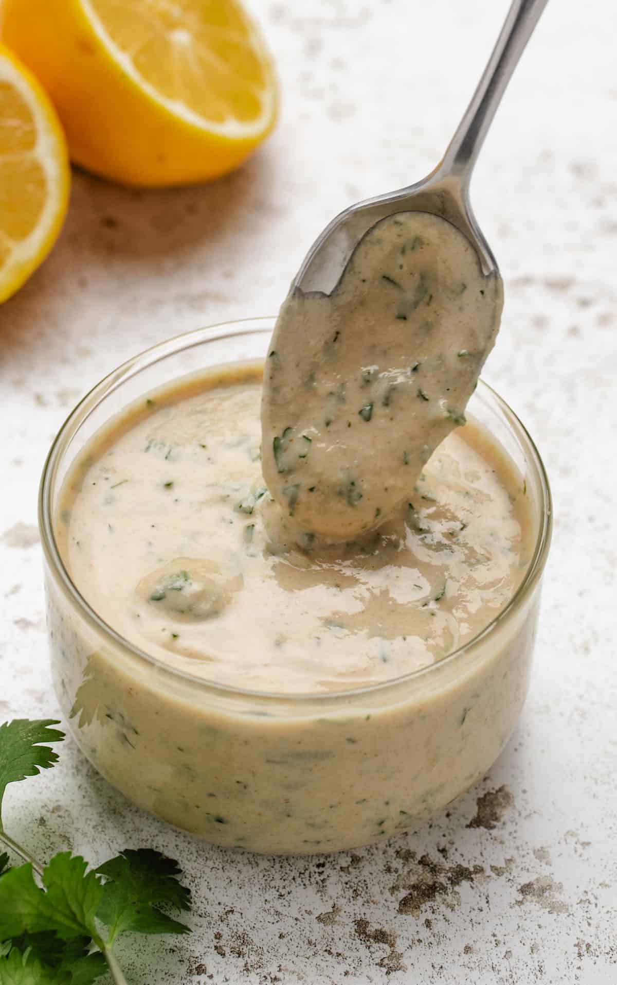 Lemon herb tahini sauce in a glass jar with a spoon dipped in the dressing.