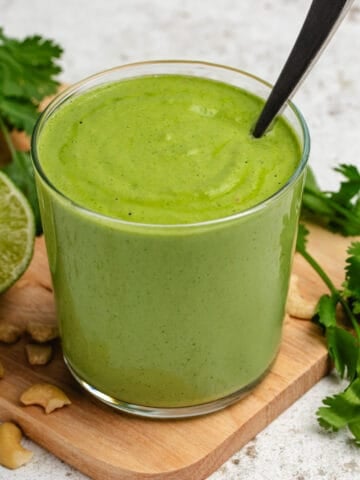 Cilantro cashew dressing in a glass with a spoon.